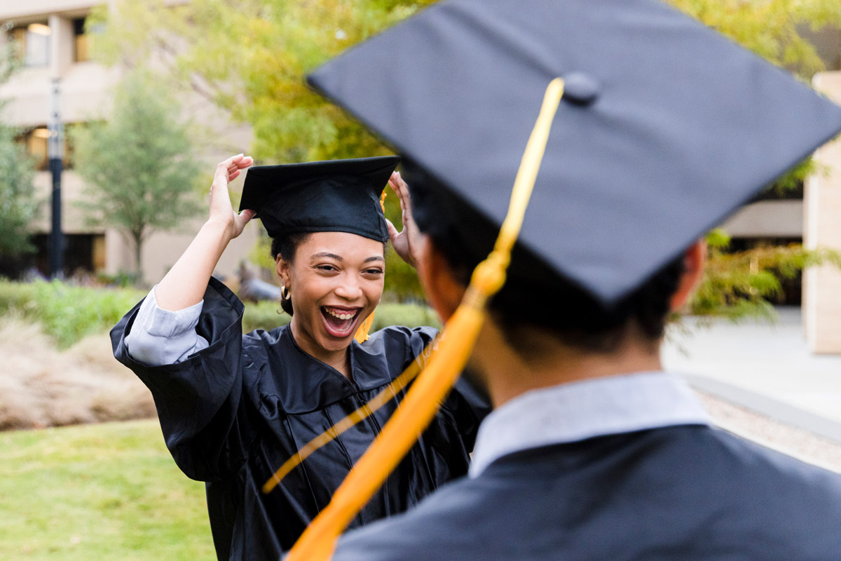 Two graduates celebrating in caps and gowns on campus